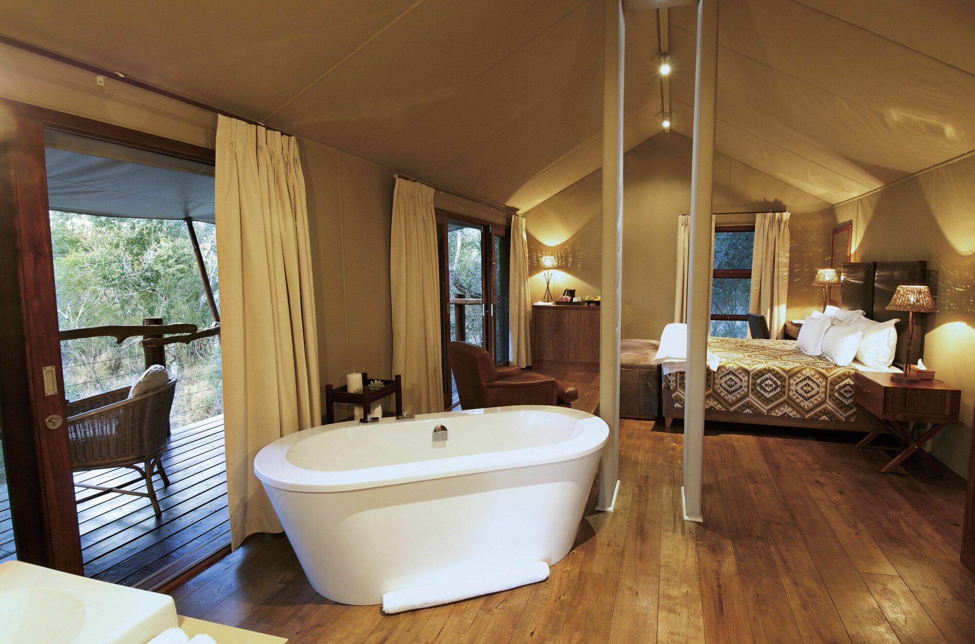 Elegant safari tent suite featuring a freestanding bathtub, cozy lounge area, king-size bed with tribal-print bedding, and private deck overlooking the bushveld.