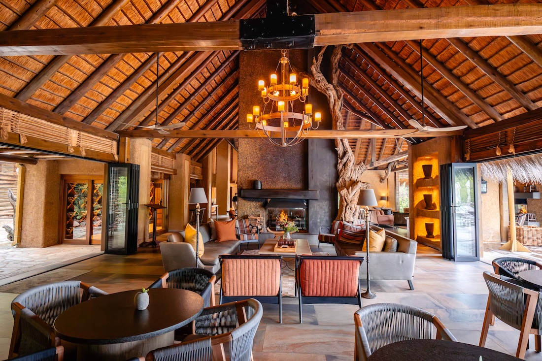 Luxury safari lodge lounge with thatched roof, cozy seating area, chandelier lighting, and a central fireplace at Kapama Private Game Reserve.